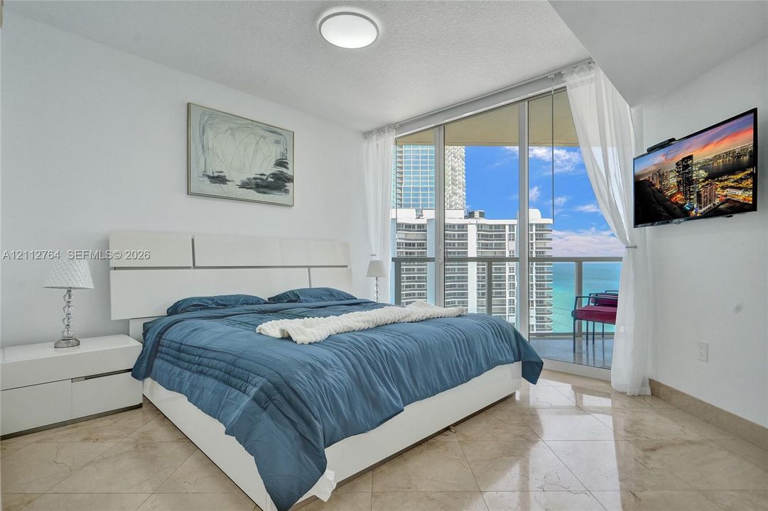 Floor-to-ceiling windows, polished stone flooring, and a private balcony featuring a glass railing