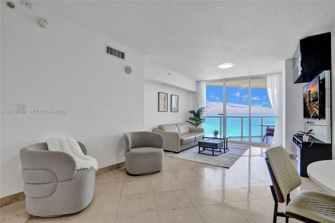 Living space featuring polished stone tile flooring, floor-to-ceiling glass paneling, and access to a private balcony