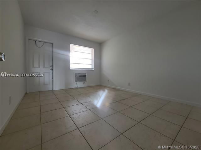 Interior room featuring neutral wall-to-wall tile flooring, a six-panel door, and a horizontal window with a built-in window air conditioning unit