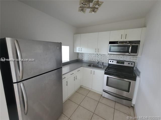 Kitchen featuring white cabinetry, stainless steel appliances, tiled backsplash, solid surface countertops, and tile flooring