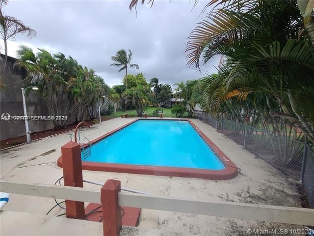 Rectangular in-ground swimming pool featuring a terra cotta border, metal handrail, concrete pool deck, perimeter fencing, and mature palm trees