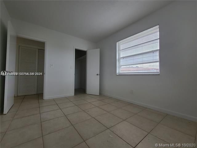 Room with tile flooring, a window featuring horizontal blinds, and a built-in closet with accordion doors
