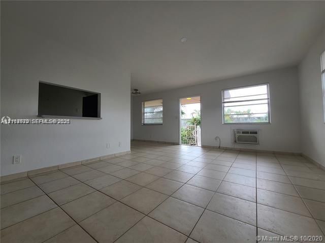 Open-concept interior featuring neutral tile flooring, multiple windows providing natural light, a pass-through wall opening, and an exterior door