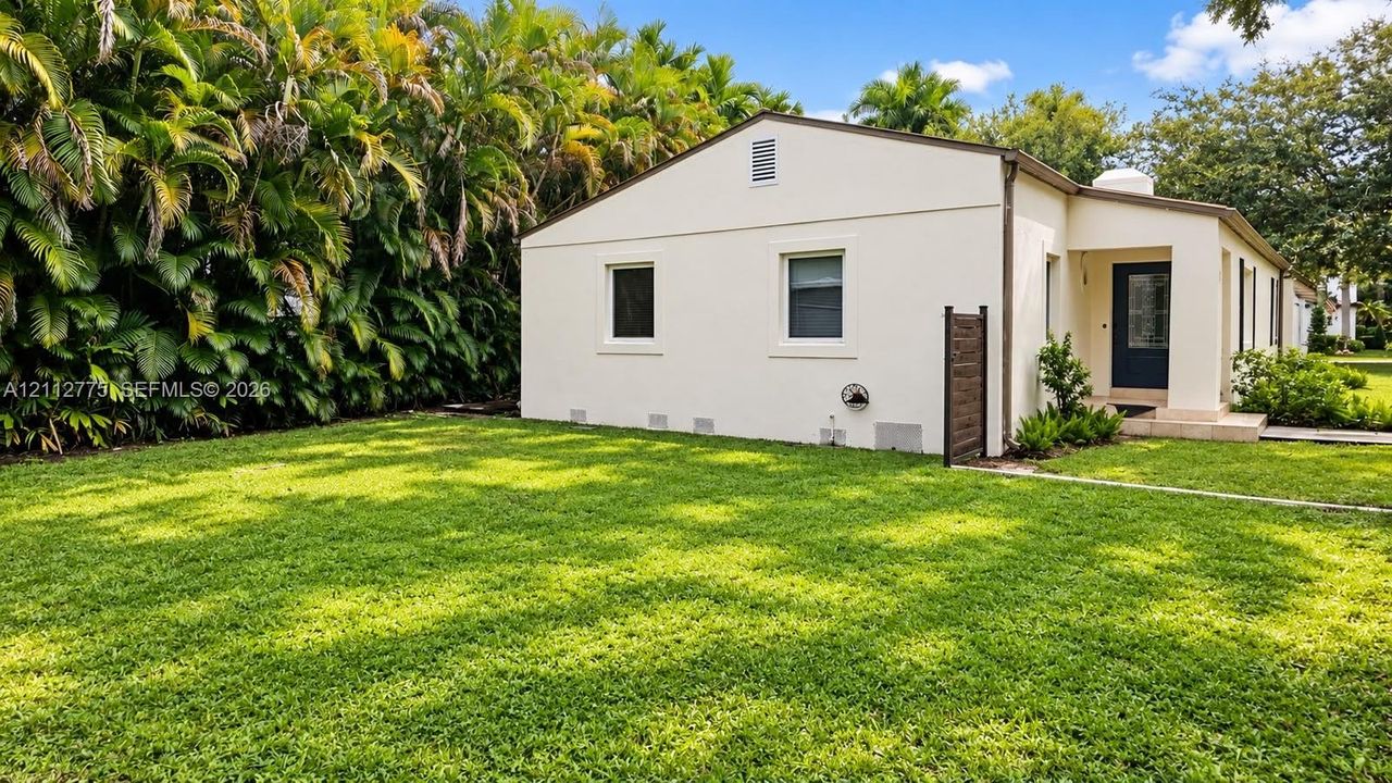 Exterior featuring a stucco facade, expansive lawn, mature perimeter hedge, and a recessed entrance with a concrete porch