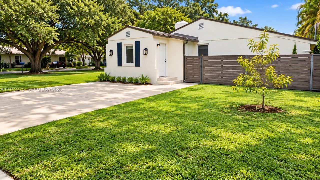 Stucco exterior featuring dark blue shutters, a concrete driveway, a horizontal wood-slat privacy fence, and mature landscaping