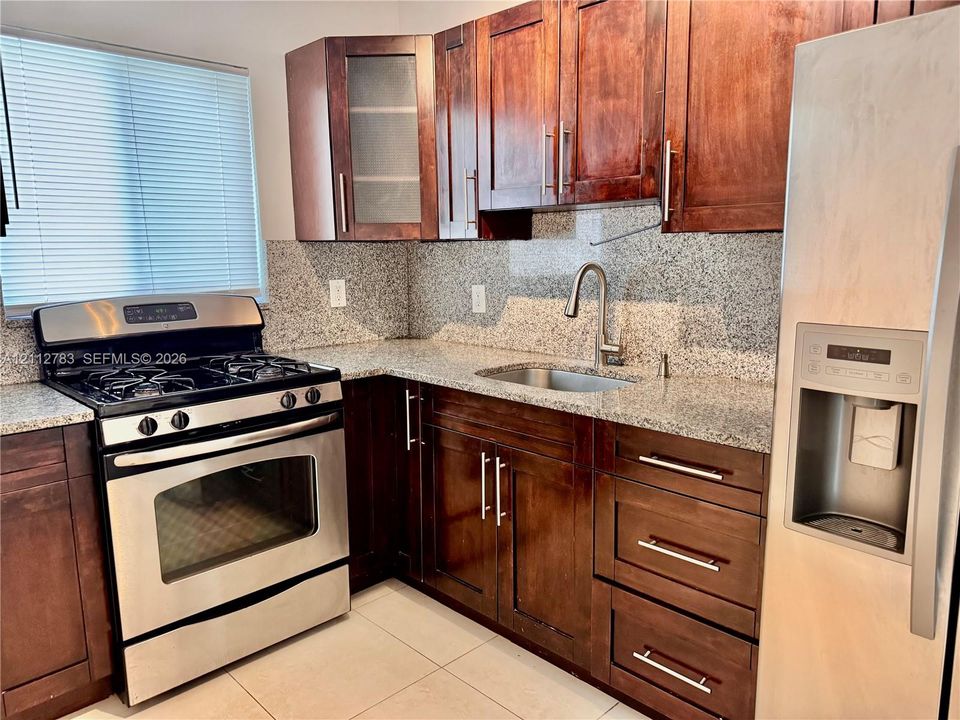 Kitchen featuring dark wood cabinetry, stone-surface countertops, full-height stone backsplash, stainless steel appliances, and high-arc faucet