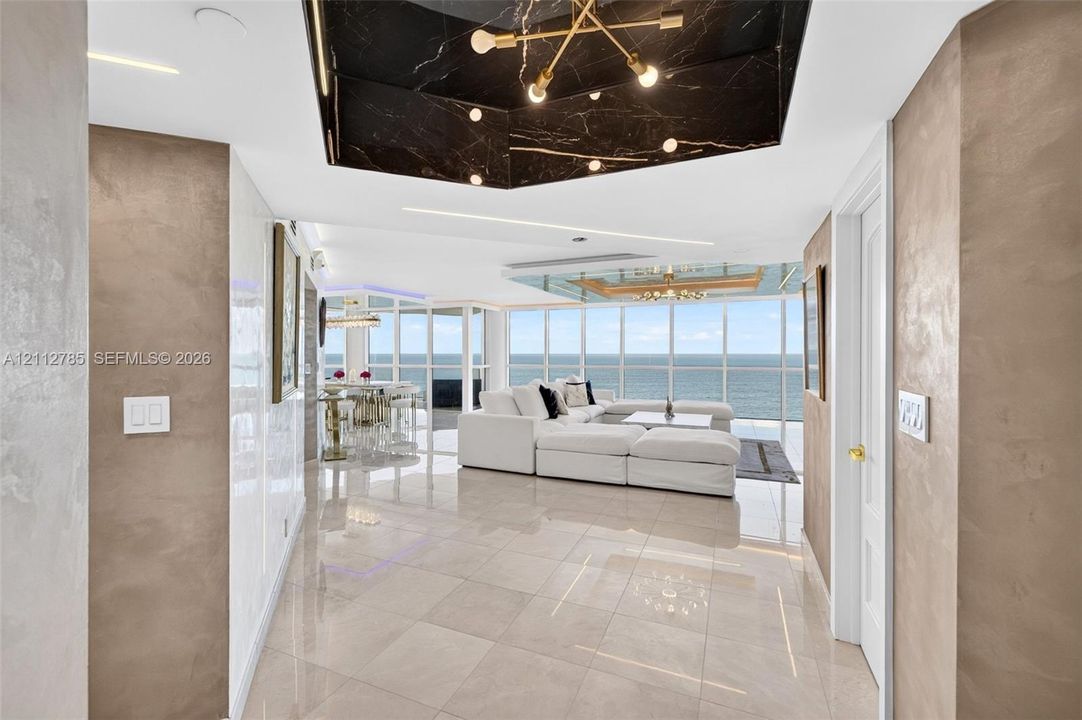 Floor-to-ceiling windows, polished tile flooring, metallic wall finishes, recessed tray ceiling with dark stone cladding, and built-in linear lighting