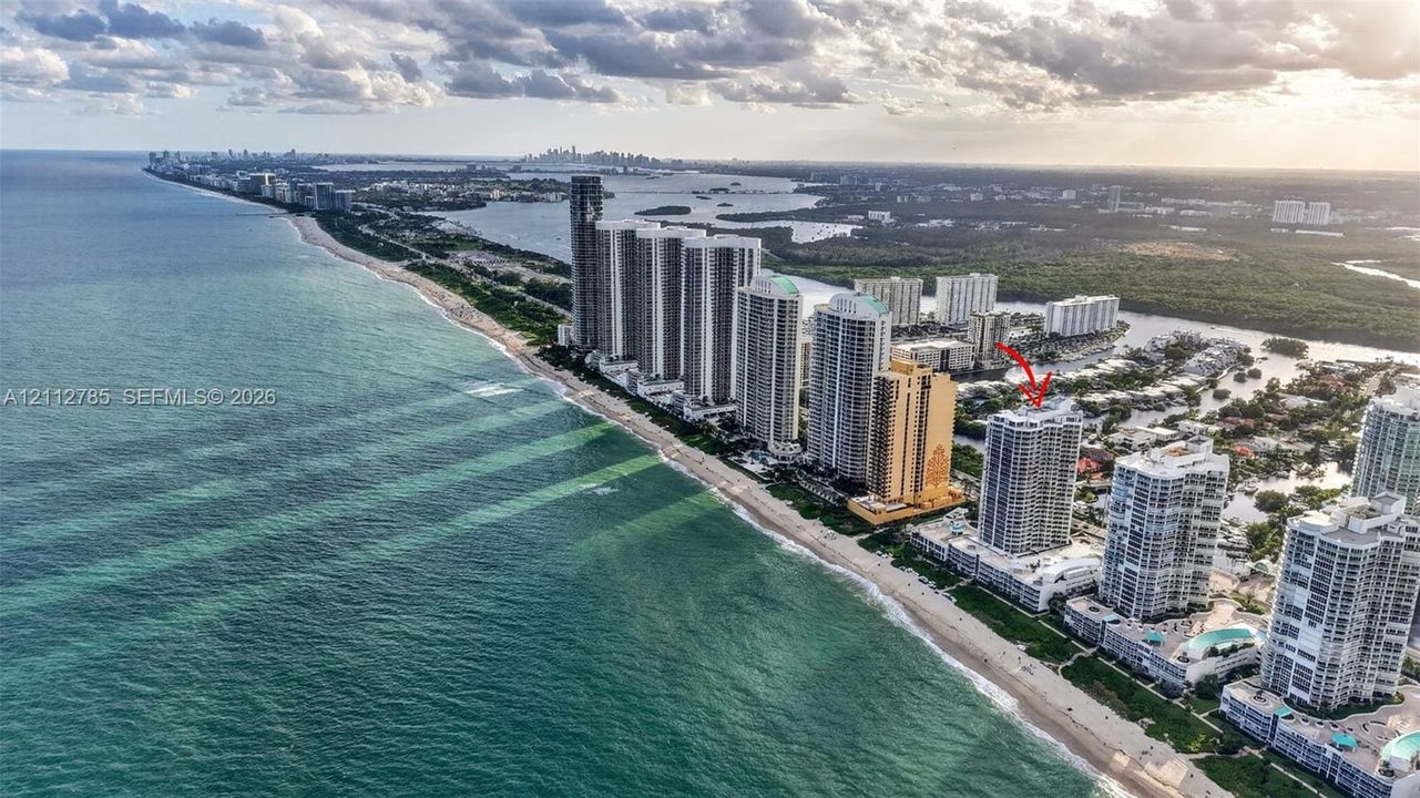 Aerial perspective featuring a high-rise residential building situated along a coastal shoreline with direct ocean frontage