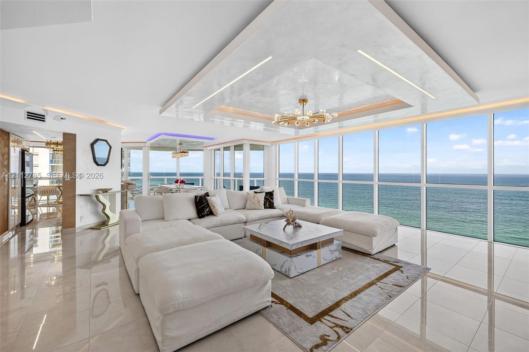 Floor-to-ceiling glass windows, recessed tray ceiling with accent lighting, polished tile flooring, and custom chandelier