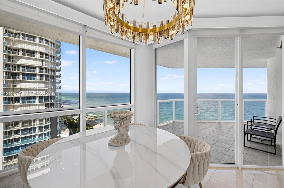 Floor-to-ceiling windows, circular multi-tiered crystal chandelier, wrap-around balcony with tiled flooring, and expansive ocean and coastal vistas