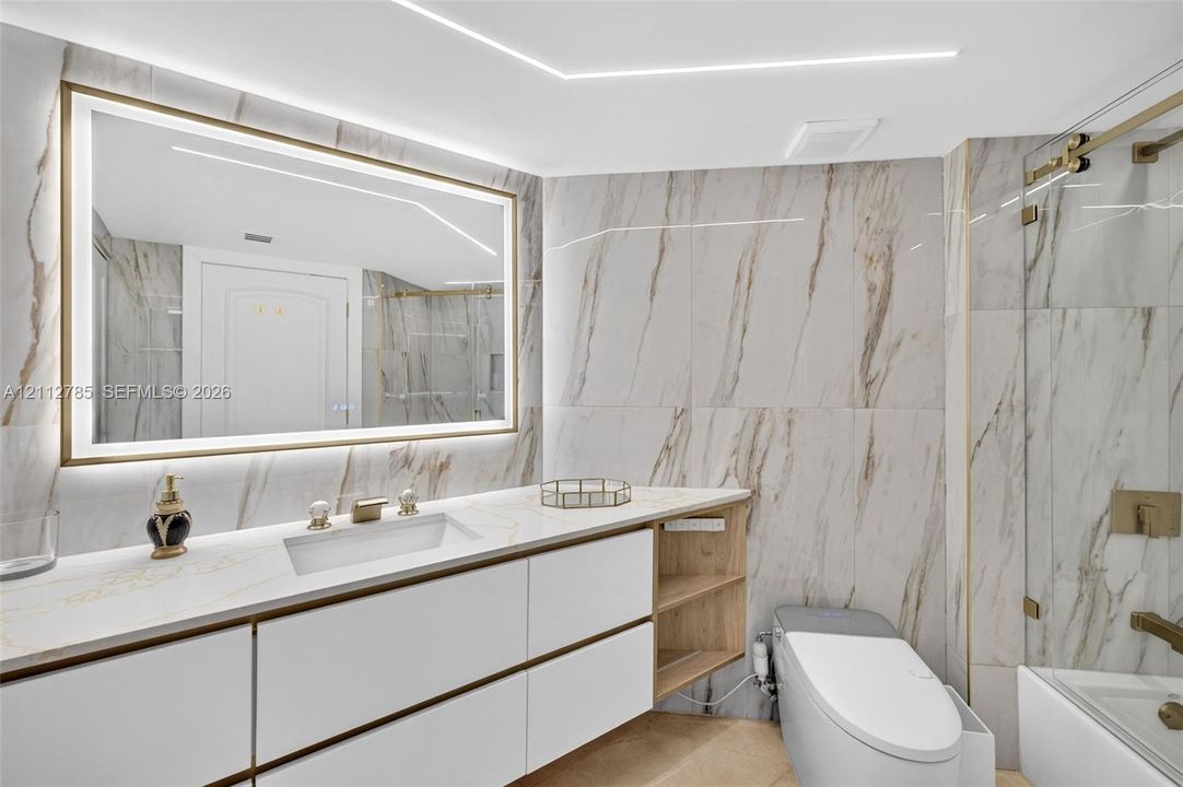 Bathroom featuring large-format stone-finish wall tile, a floating vanity with integrated cabinetry, an illuminated vanity mirror, and a glass-enclosed shower with metallic hardware