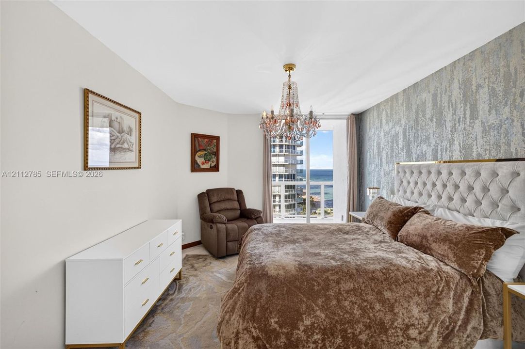 Textured accent wall, crystal chandelier, and floor-to-ceiling glass door opening to a private balcony
