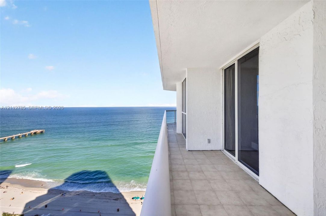 Covered balcony featuring tiled flooring, a glass panel railing, and white stucco exterior wall with sliding glass door access