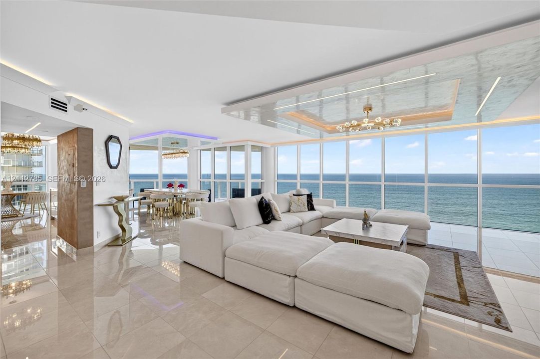 Floor-to-ceiling windows featuring ocean horizon, recessed tray ceiling with integrated lighting, polished stone-finish flooring, and architectural metallic-finish wall paneling