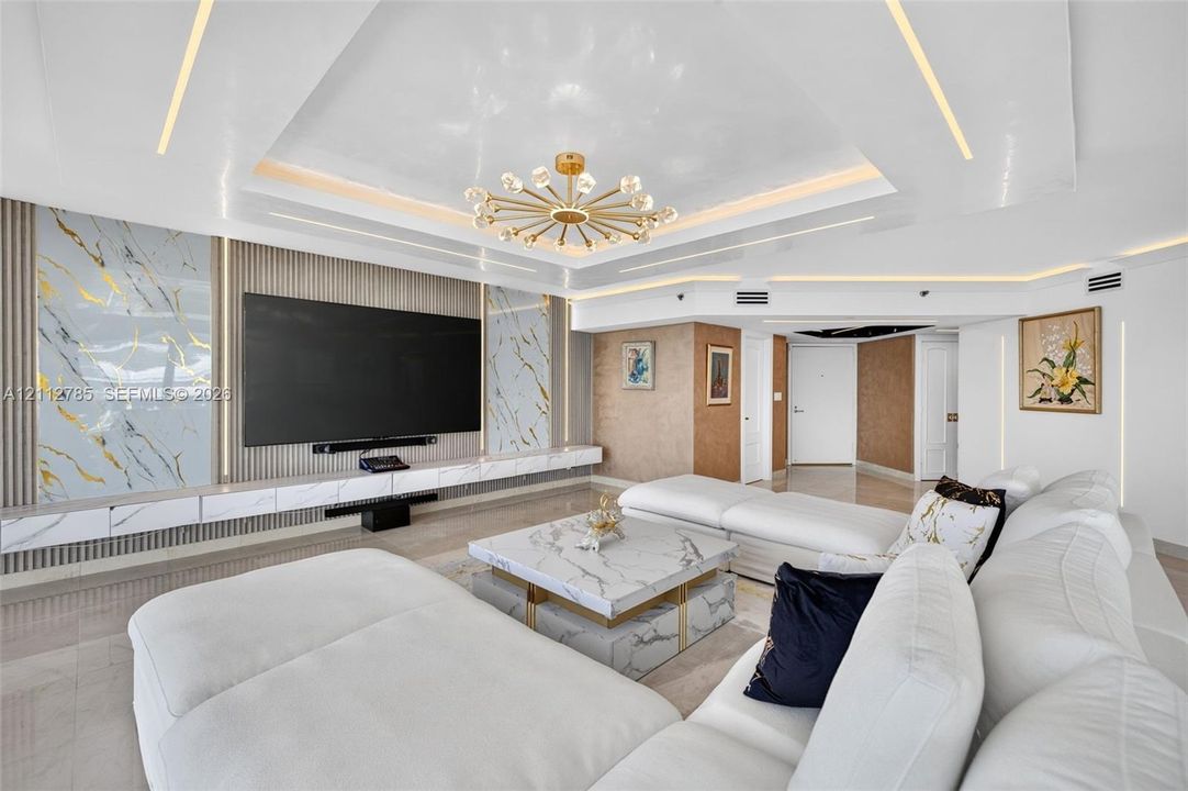 Tray ceiling featuring integrated perimeter lighting, custom stone-panel wall accents, recessed linear lighting, and a modern multi-arm chandelier