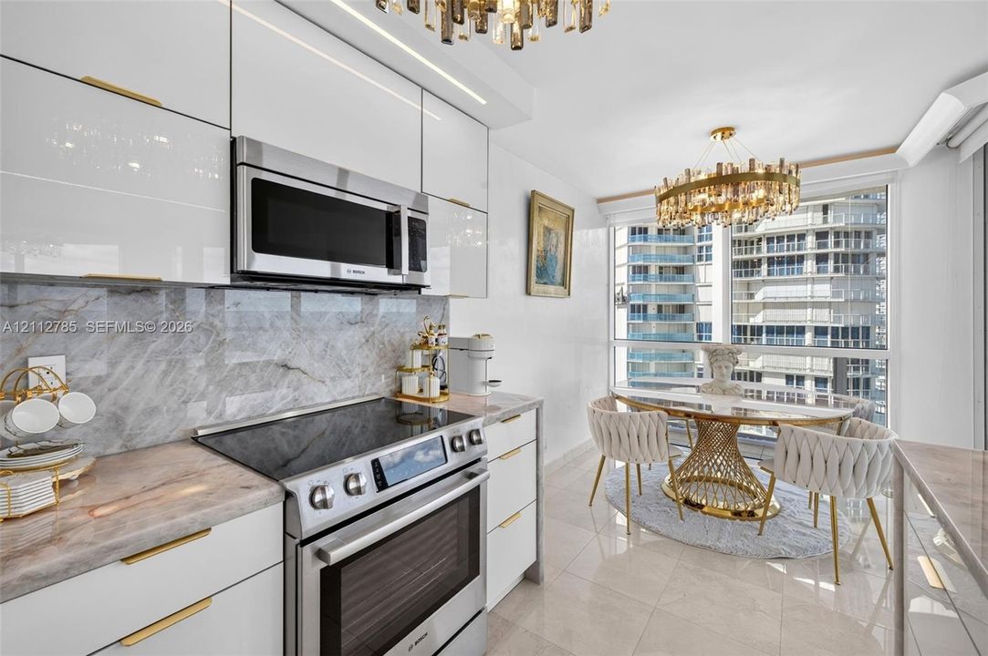 Kitchen featuring high-gloss white cabinetry, gold-tone hardware, stone-surface countertops, stone-tile backsplash, and integrated stainless steel appliances