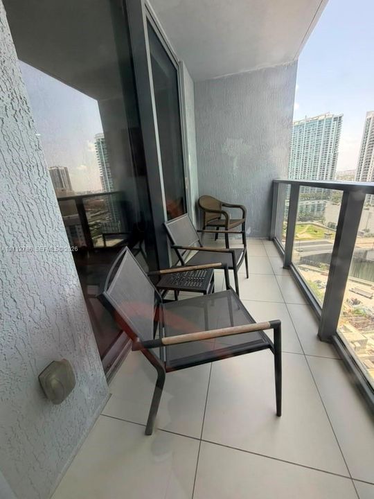 Covered balcony featuring large-format ceramic floor tiles, glass-panel railing, and floor-to-ceiling glass sliding doors