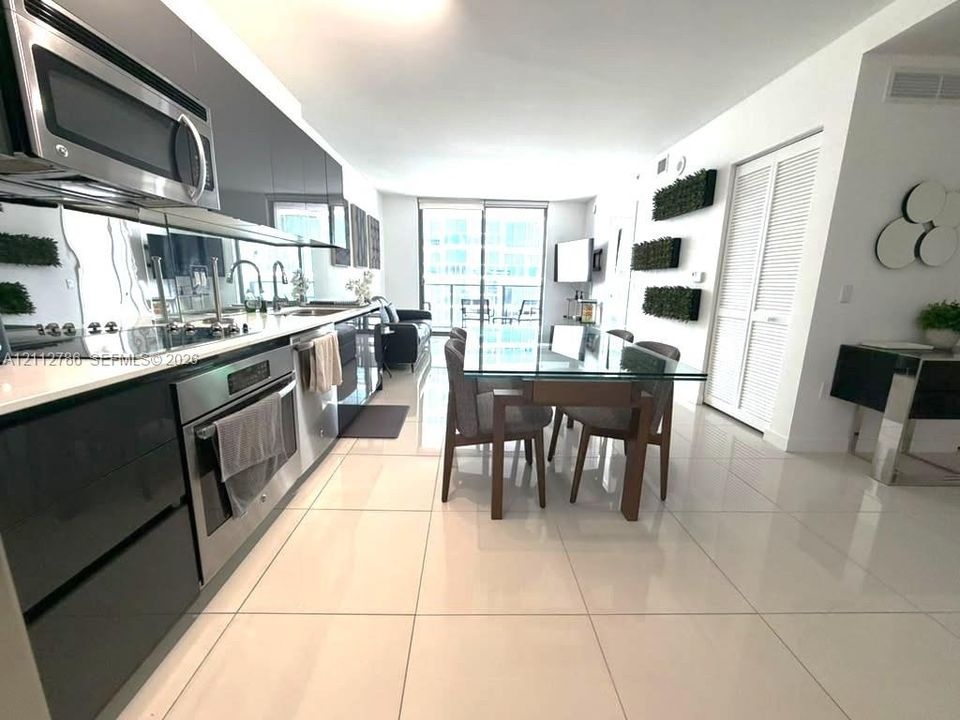 Kitchen featuring high-gloss cabinetry, stainless steel appliances, and solid-surface countertops, complemented by large-format tile flooring and floor-to-ceiling glass doors