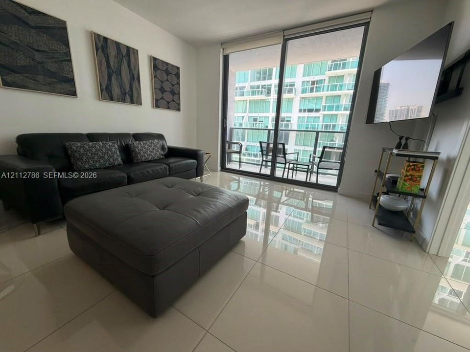 Floor-to-ceiling sliding glass doors, private balcony with metal railing, and large-format polished tile flooring