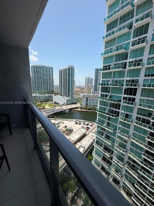 Private balcony with glass and metal railing, overlooking urban high-rise architecture and waterfront