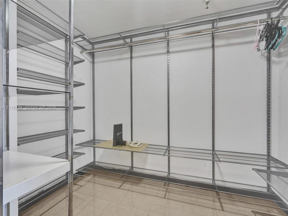 Walk-in storage space featuring adjustable metal wire shelving, integrated hanging rods, and polished tile flooring