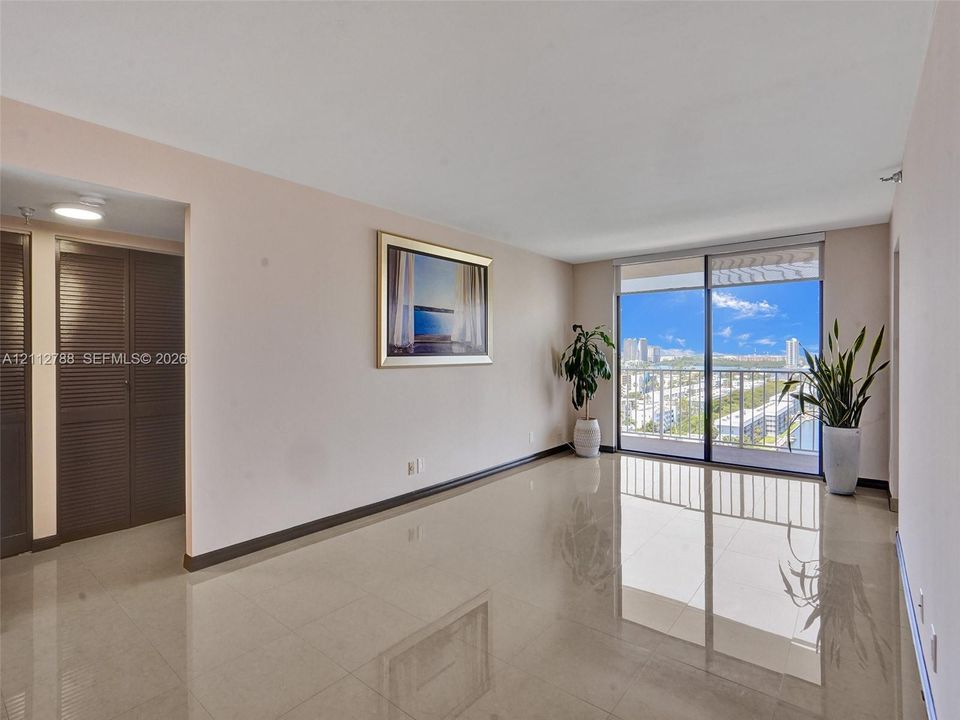 Living area featuring polished tile flooring, floor-to-ceiling glass sliding doors, a metal balcony railing, and built-in louvered closet doors