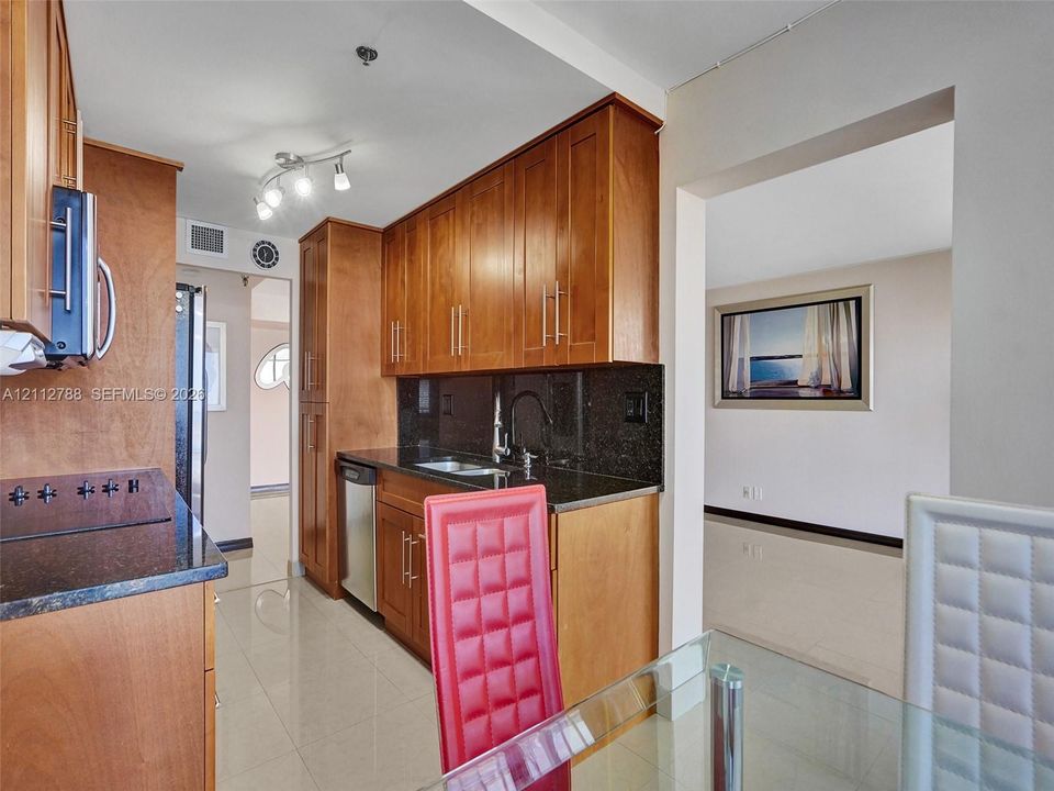Kitchen featuring natural finish wood cabinetry, dark stone countertops, stainless steel appliances, and tile flooring
