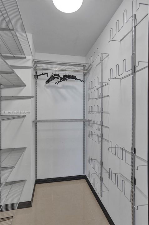 Walk-in storage space featuring adjustable metal wire shelving, dedicated rack organization for footwear, ceiling-mounted lighting, and tile flooring