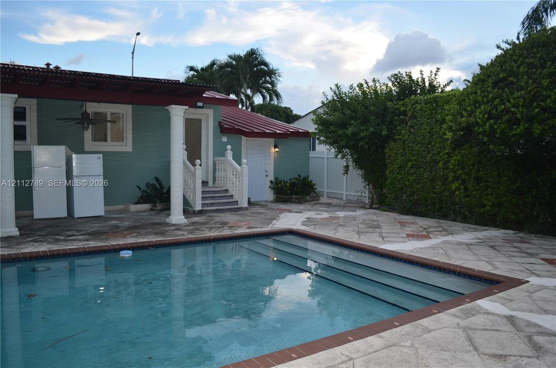 Exterior area featuring a swimming pool with tiered entry steps, stone paver decking, a covered patio with columns, and a metal roof