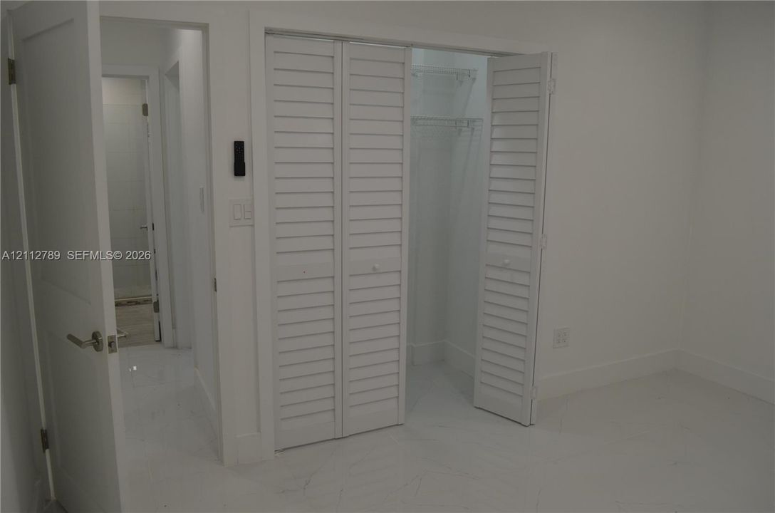 Closet featuring white louvered bifold doors and built-in shelving, complemented by polished stone flooring and a solid-core interior door with satin nickel hardware
