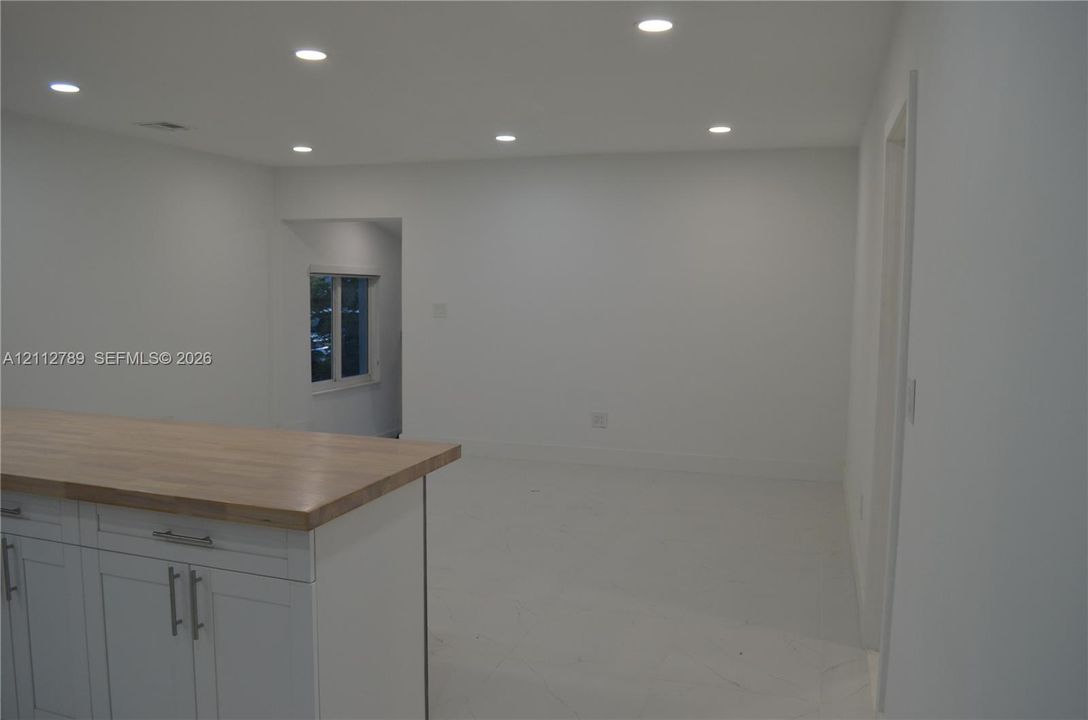 Kitchen island featuring white Shaker-style cabinetry, wood-finish countertop, recessed lighting, and tile flooring