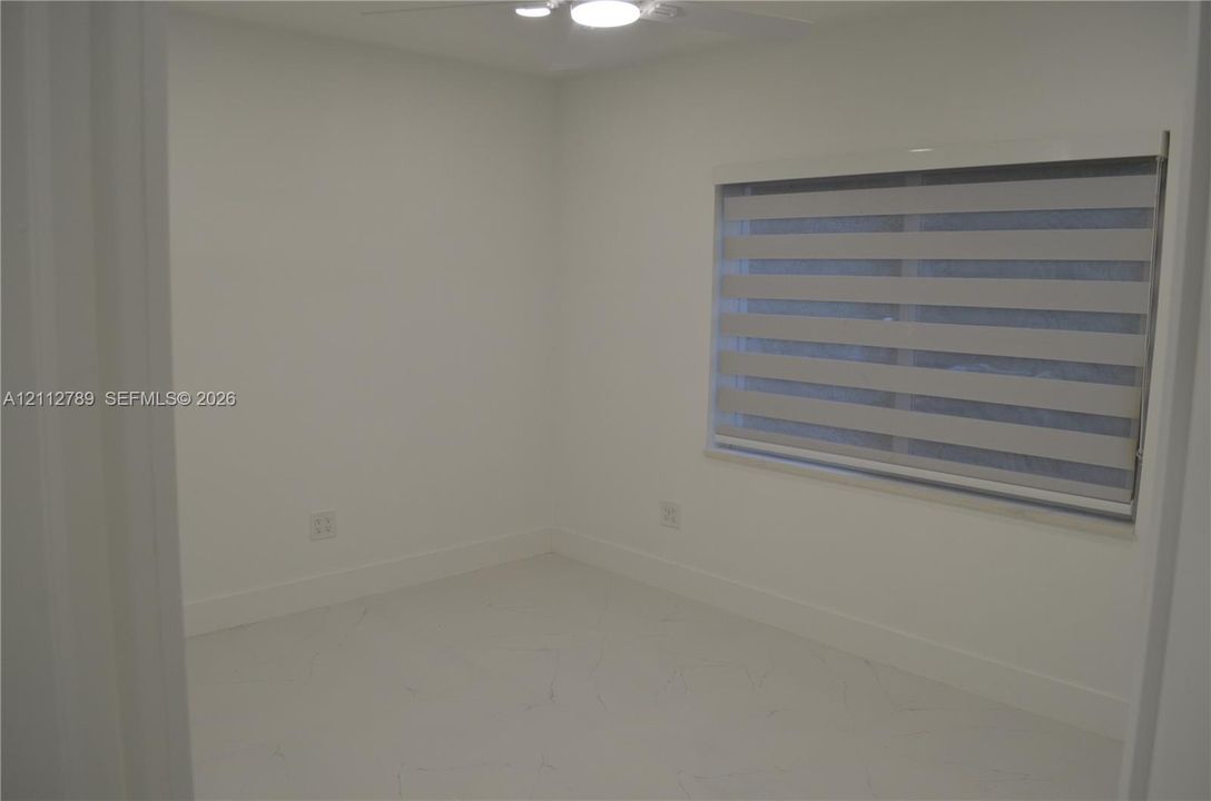 Neutral interior space featuring polished tile flooring, crisp white wall finishes, a ceiling-mounted light fixture, and horizontal zebra-style window blinds