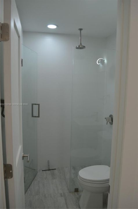 Walk-in shower featuring a frameless glass enclosure, ceiling-mounted rainfall showerhead, and stone-finish tile flooring
