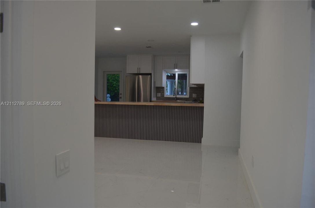Kitchen featuring white cabinetry, stainless steel refrigerator, recessed lighting, and a peninsula with a vertical-slatted base and wood-finish countertop