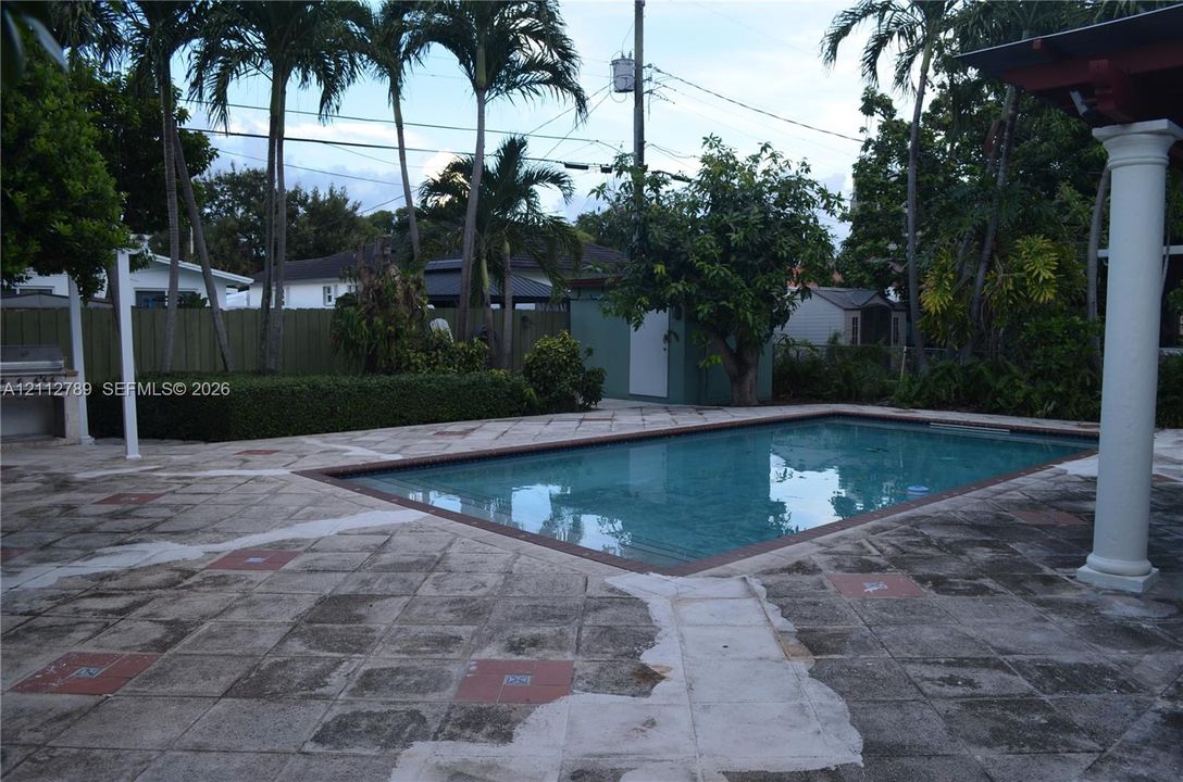 Outdoor area featuring a rectangular pool, stone-paver patio, built-in masonry grill, covered terrace with columns, and privacy fencing