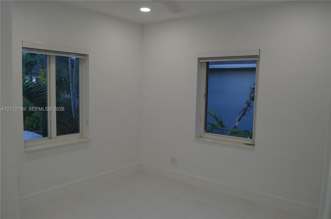 Neutral interior space featuring white walls, recessed ceiling lighting, dual windows with wide casings, and white tile flooring