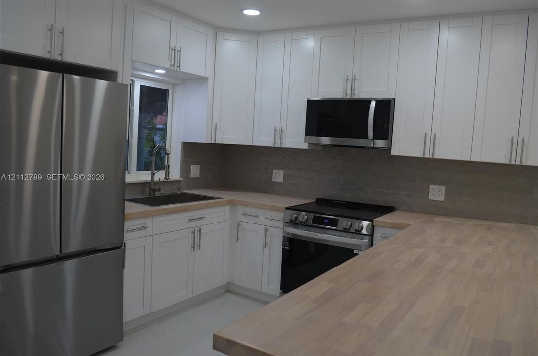 Kitchen featuring white shaker-style cabinetry, wood-surface countertops, stainless steel appliances, a tile backsplash, and a gooseneck faucet