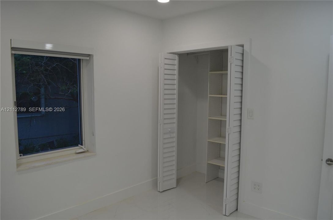 Interior space featuring high-gloss flooring, a recessed window with a stone sill, and a closet with white louvered bifold doors and integrated shelving