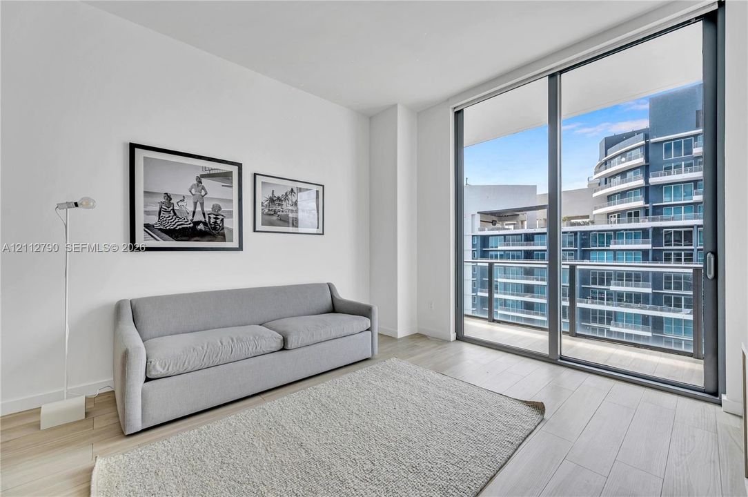 Floor-to-ceiling glass sliding doors, light-toned wood-finish flooring, and a private balcony with metal railings