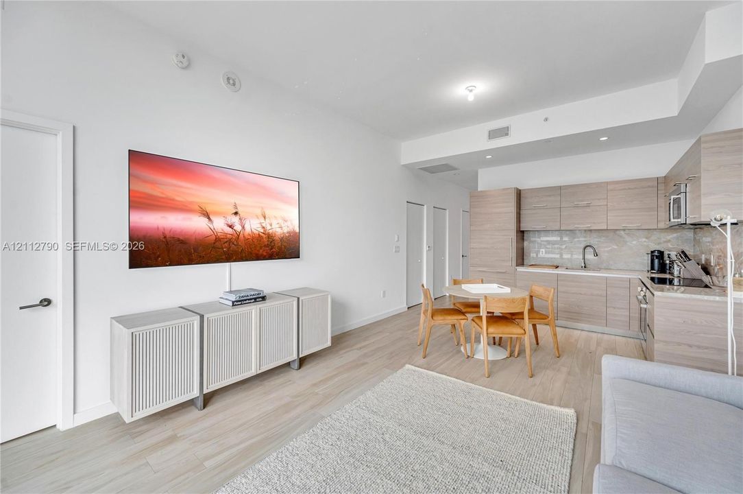 Open-concept interior featuring light wood-finish flooring, cabinetry with a horizontal grain finish, stone-surface countertops, and recessed ceiling lighting