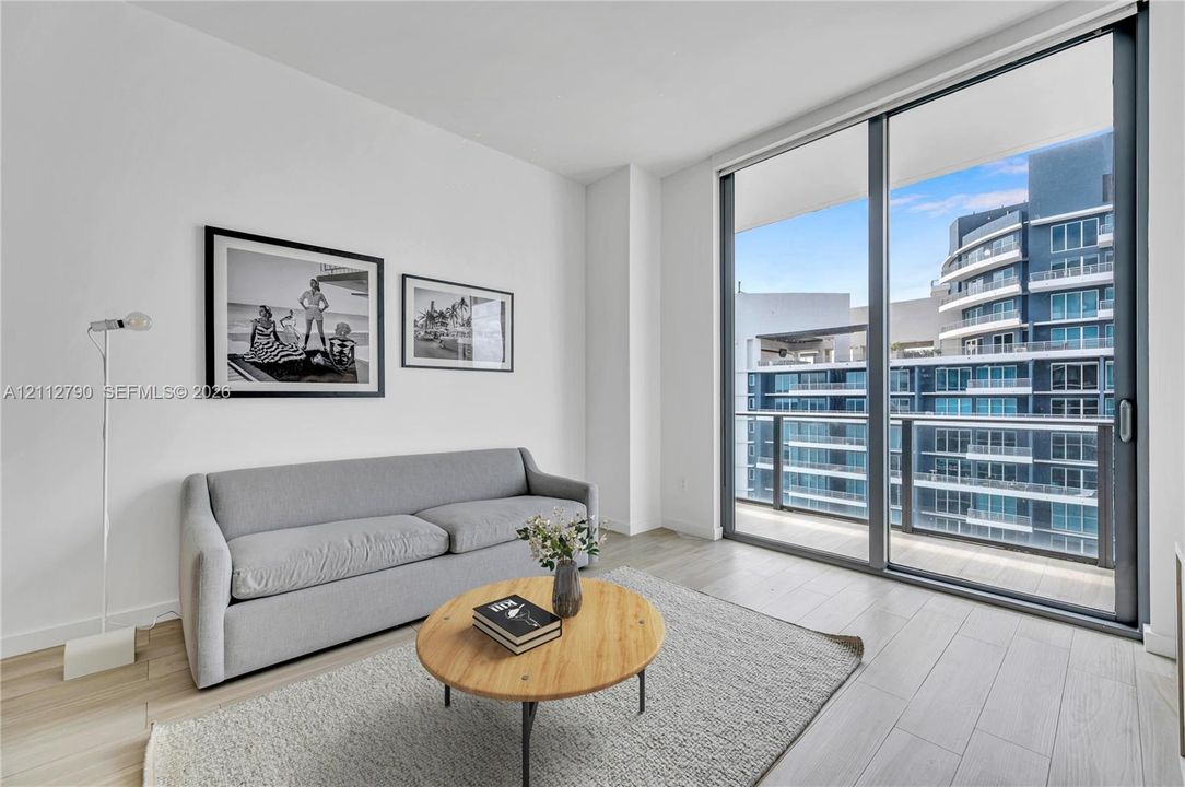 Floor-to-ceiling glass sliding doors, wood-finish flooring, and a private balcony with metallic railing