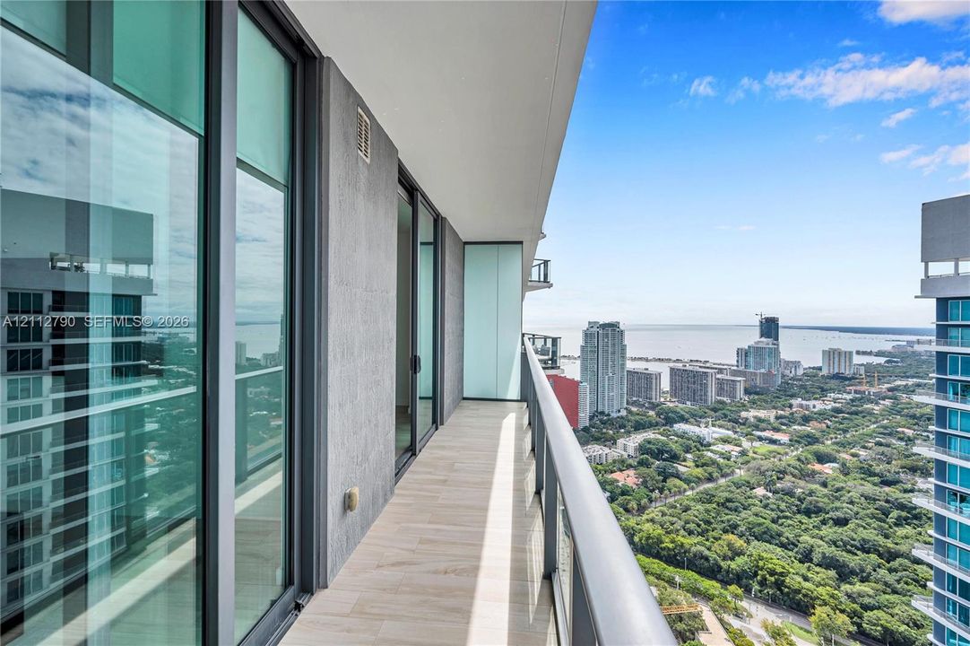 Private balcony featuring tile flooring, floor-to-ceiling glass doors, and metal railings with expansive water and urban scenery