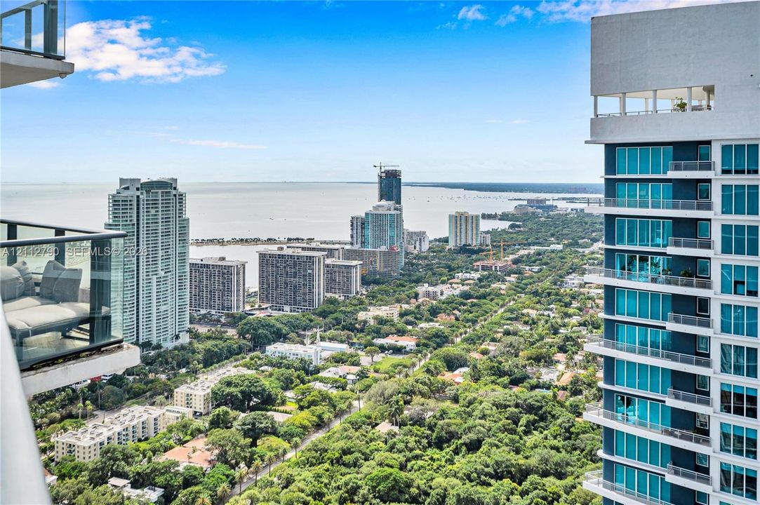 Elevated balcony with glass railings overlooking a coastal cityscape, high-rise architecture, and expansive water scenery