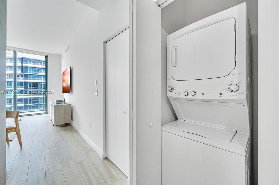 Stackable laundry unit housed within a dedicated closet, featuring light-toned wood-finish flooring and full-height glass windows