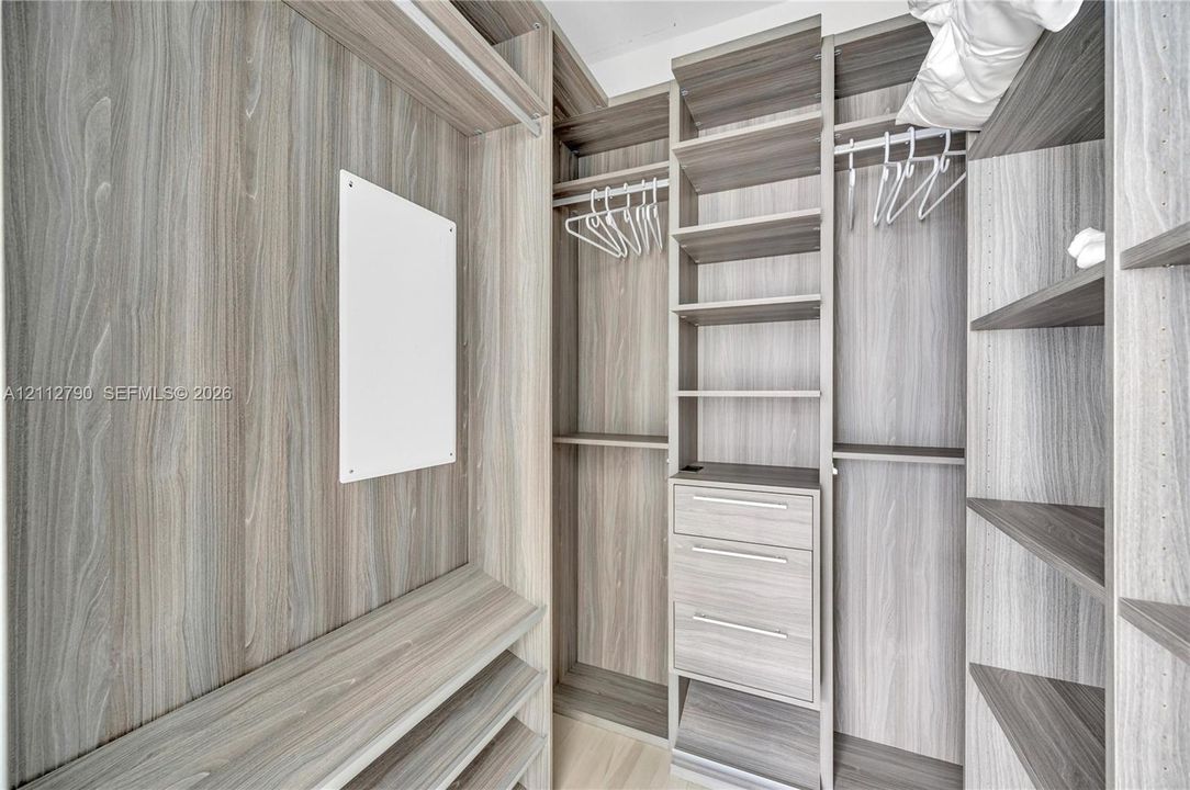 Custom wood-finish closet storage system featuring integrated hanging rods, multi-level shelving, and built-in drawers with metallic hardware