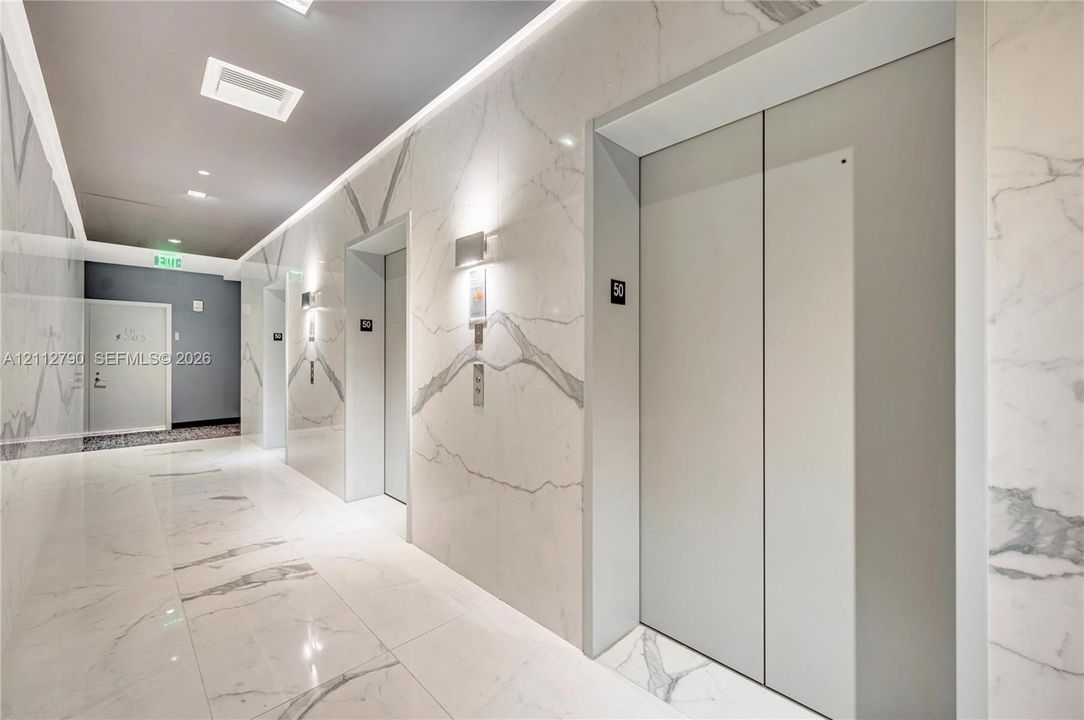 Elevator lobby featuring floor-to-ceiling stone wall cladding, polished stone flooring, recessed ceiling lighting, and minimalist metal elevator doors