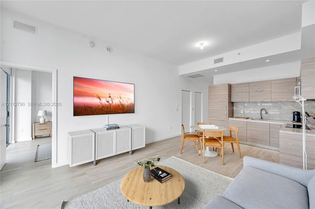 Open-concept living space featuring wood-finish flooring, flat-panel cabinetry, a light-toned stone backsplash, and recessed ceiling lighting