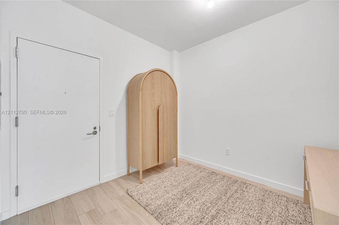 Neutral-toned interior featuring wood-finish flooring, smooth-finish walls, and a solid-core swing door with brushed metal hardware