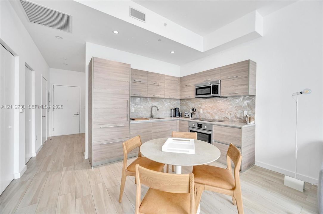 Kitchen featuring wood-finish cabinetry, stone backsplash, integrated appliances, and wood-finish flooring