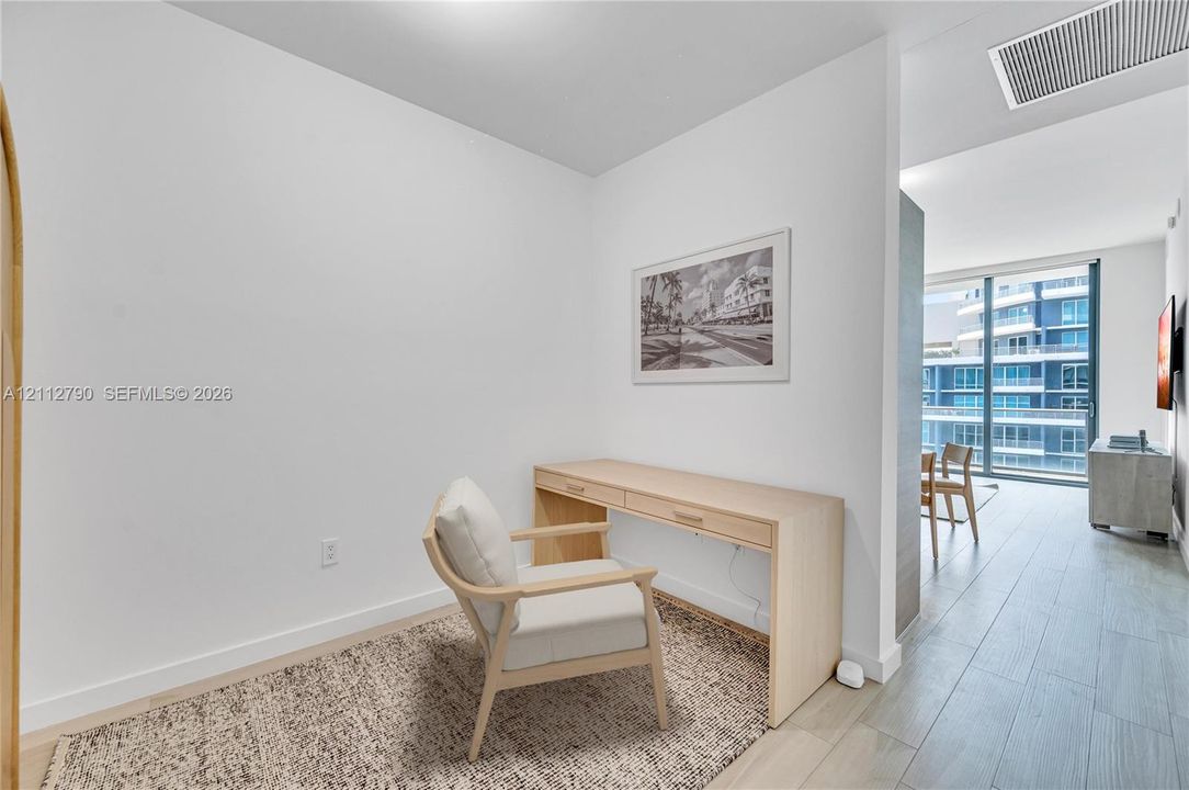 Built-in light-tone wood desk with integrated drawers, wood-finish flooring, and floor-to-ceiling glass sliding doors
